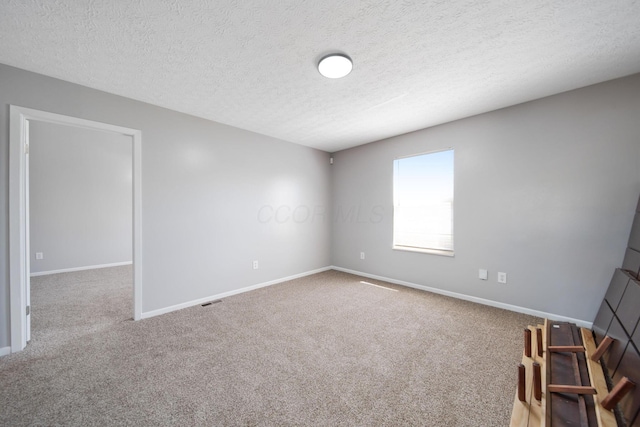 spare room with a textured ceiling, baseboards, and carpet
