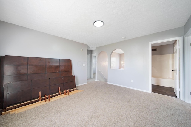 unfurnished living room with carpet floors, arched walkways, and baseboards