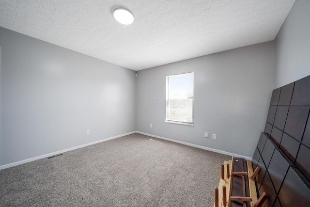 carpeted spare room with baseboards, a textured ceiling, and visible vents
