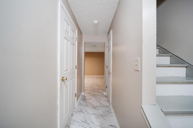 hall featuring stairway, a textured ceiling, baseboards, and marble finish floor