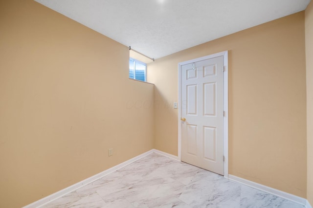 below grade area with baseboards, a textured ceiling, and marble finish floor