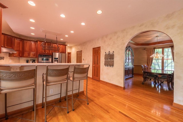8884 Filiz Ln, Powell, OH 43065 - kitchen with appliances with stainless steel finishes, arched walkways, light wood-type flooring, recessed lighting, and under cabinet range hood