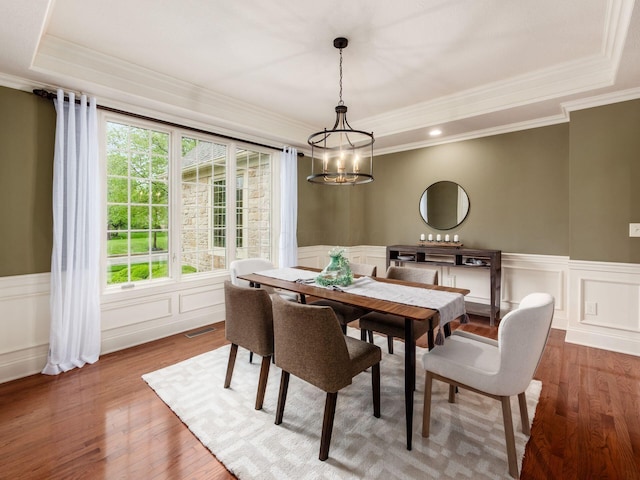 dining space with a chandelier, a raised ceiling, wood finished floors, crown molding, and a decorative wall