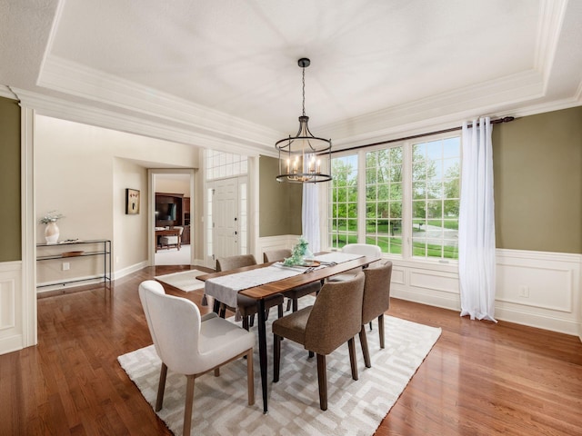 dining area featuring a chandelier, wood finished floors, a raised ceiling, ornamental molding, and a wainscoted wall