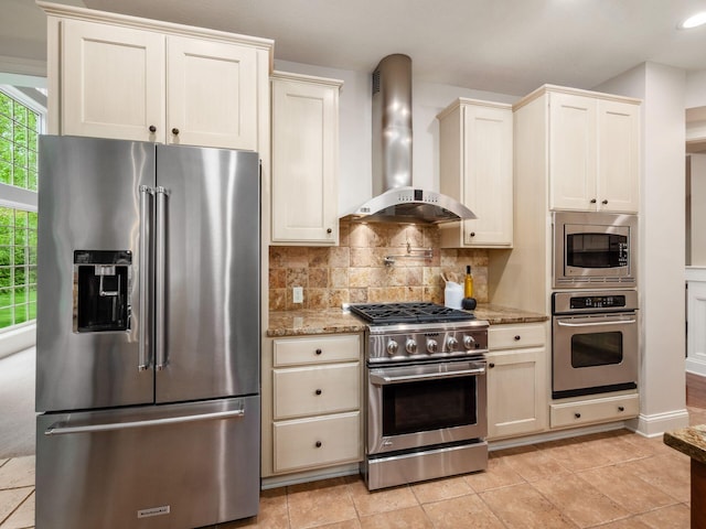 kitchen featuring high quality appliances, wall chimney range hood, backsplash, light stone counters, and recessed lighting
