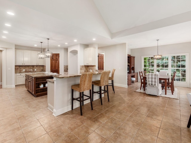 kitchen featuring recessed lighting, tasteful backsplash, white cabinets, light stone countertops, and a kitchen bar