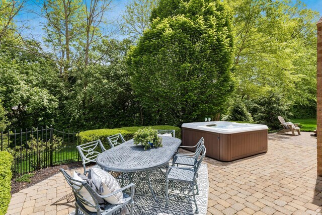 view of patio with a hot tub, outdoor dining area, fence, and view of wooded area