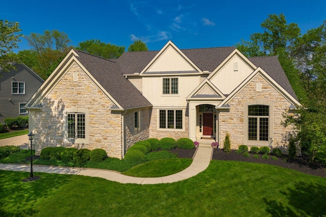 view of front facade with stone siding, a front yard, a shingled roof, and board and batten siding