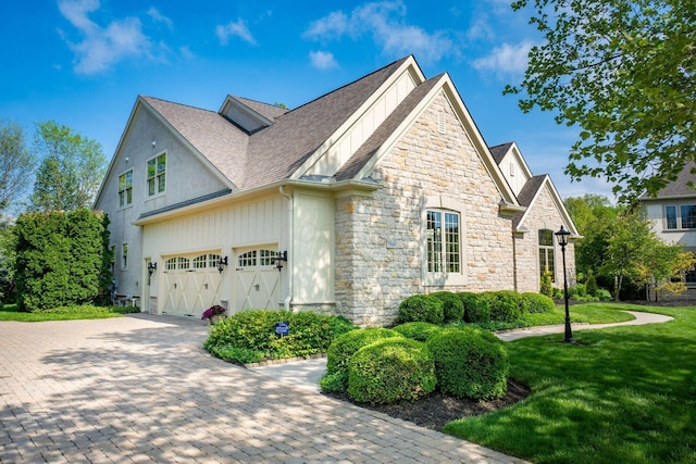 view of home's exterior featuring stone siding, a yard, a garage, roof with shingles, and driveway