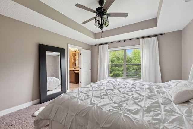 bedroom with carpet, a ceiling fan, a tray ceiling, connected bathroom, and baseboards
