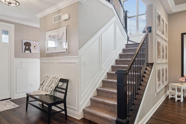staircase with a decorative wall, wood finished floors, visible vents, crown molding, and wainscoting