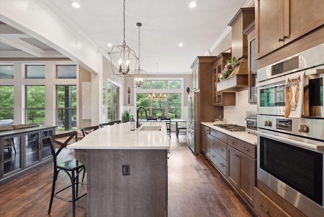 kitchen with a sink, stainless steel appliances, ornamental molding, a kitchen bar, and a notable chandelier