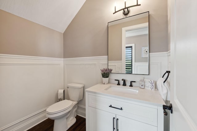 half bathroom featuring vanity, toilet, a decorative wall, and wainscoting