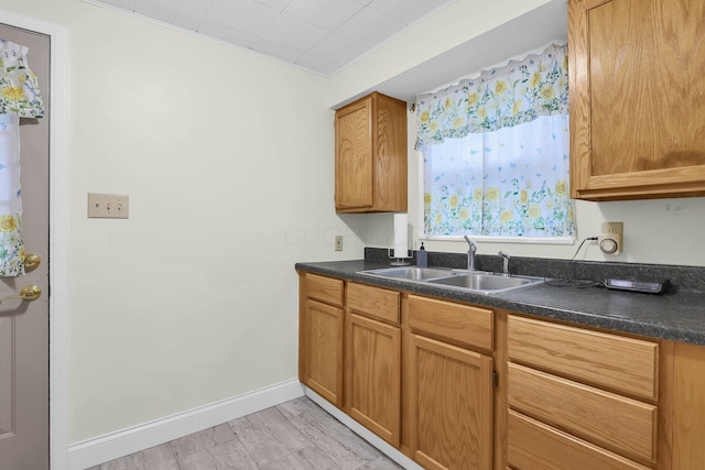 kitchen featuring a sink, dark countertops, baseboards, and brown cabinets