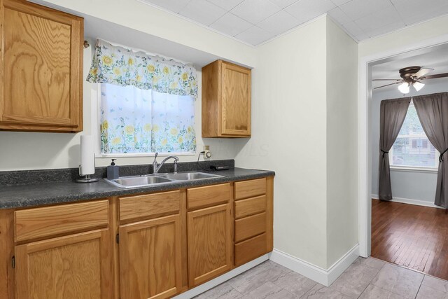 kitchen with a sink, dark countertops, a ceiling fan, and baseboards
