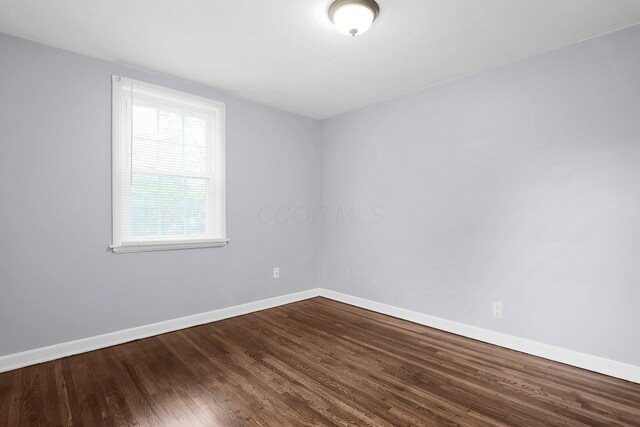 spare room with dark wood-style flooring and baseboards