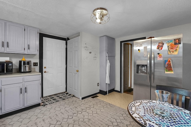 kitchen with stainless steel fridge with ice dispenser, black microwave, light countertops, a textured ceiling, and baseboards