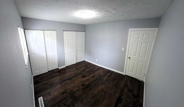 3087 Woodway Rd, Columbus, OH 43207 - unfurnished bedroom featuring two closets, dark wood finished floors, a textured ceiling, and baseboards