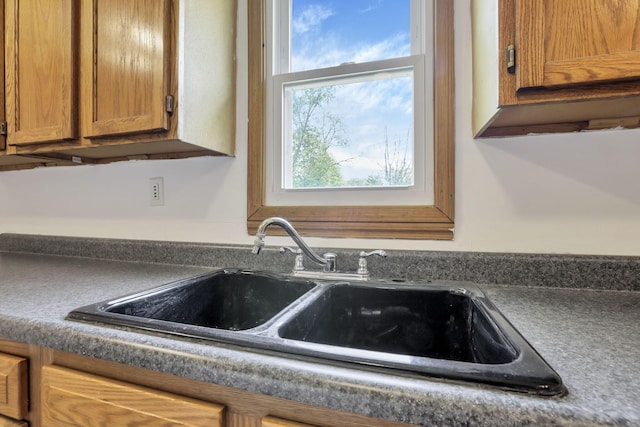 interior details with a sink, brown cabinetry, and dark countertops