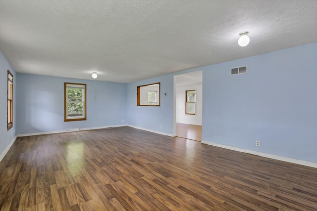 unfurnished room with a textured ceiling, visible vents, baseboards, and dark wood-type flooring