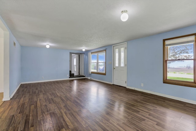 unfurnished living room featuring a wealth of natural light, baseboards, and dark wood-style floors