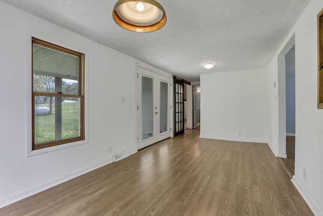 empty room with french doors, wood finished floors, a textured ceiling, visible vents, and baseboards