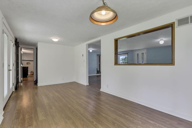empty room featuring a barn door, baseboards, visible vents, and wood finished floors
