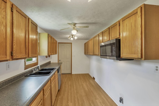 kitchen with a sink, brown cabinetry, light wood-style flooring, a ceiling fan, and appliances with stainless steel finishes