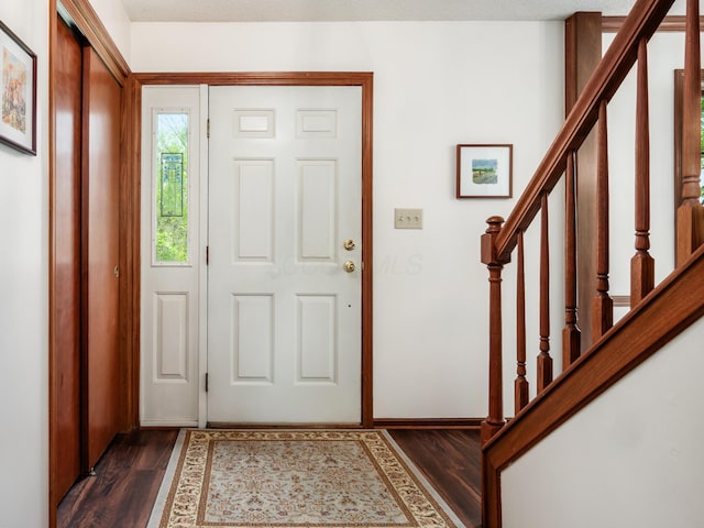 foyer with dark wood-type flooring, stairs, and baseboards