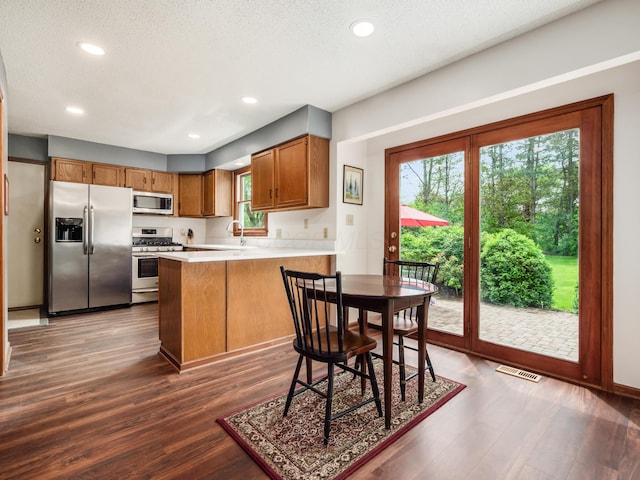 kitchen featuring appliances with stainless steel finishes, a peninsula, wood finished floors, brown cabinets, and recessed lighting