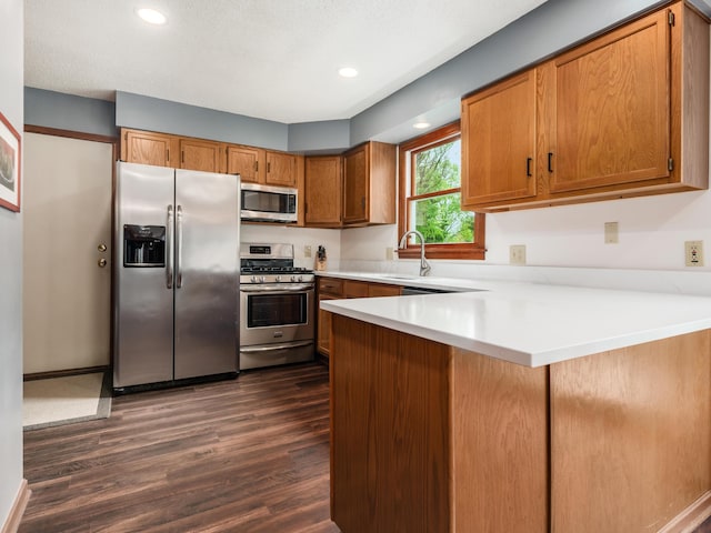 kitchen with stainless steel appliances, a peninsula, dark wood-style floors, brown cabinets, and light countertops