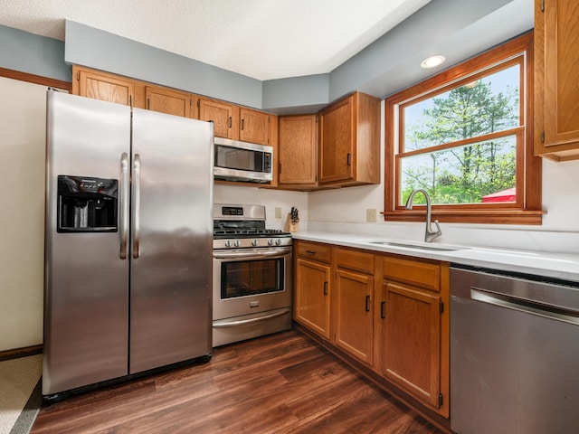 kitchen with stainless steel appliances, a sink, light countertops, brown cabinets, and dark wood-type flooring