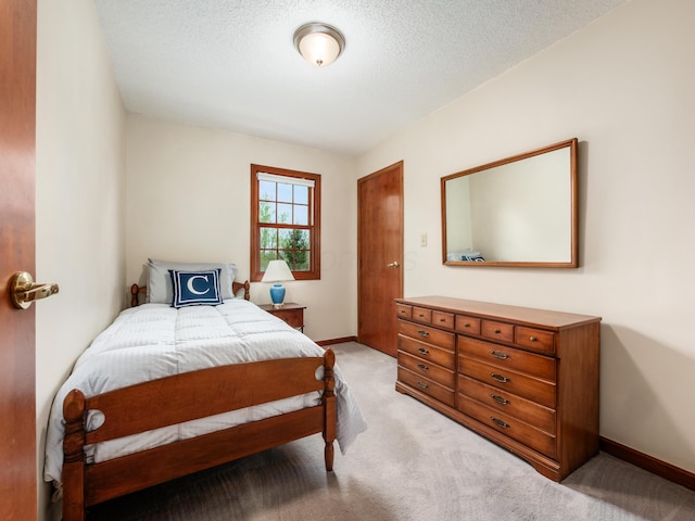 bedroom with light carpet, baseboards, and a textured ceiling