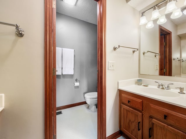 bathroom with toilet, a textured ceiling, vanity, and baseboards