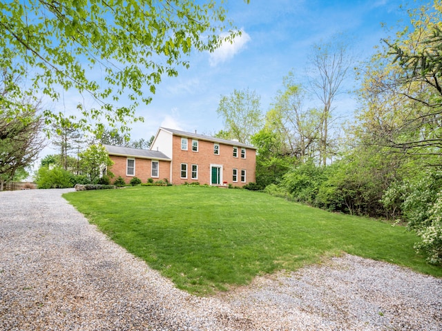 rear view of house featuring a lawn, brick siding, and gravel driveway