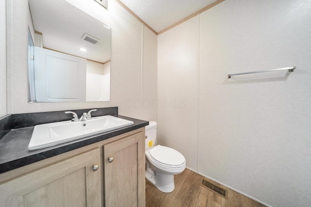 bathroom with vanity, toilet, wood finished floors, and visible vents