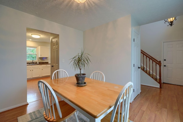dining area with stairs, light wood-style floors, a chandelier, a textured ceiling, and baseboards