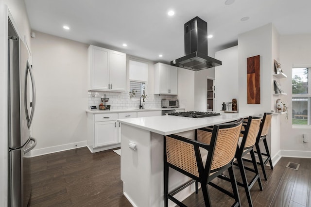kitchen featuring visible vents, freestanding refrigerator, a breakfast bar, island range hood, and a sink