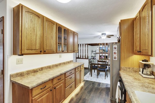 kitchen featuring brown cabinets, ceiling fan, dark wood finished floors, freestanding refrigerator, and glass insert cabinets