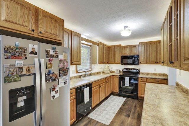 kitchen with light countertops, dark wood-style flooring, black appliances, and a sink