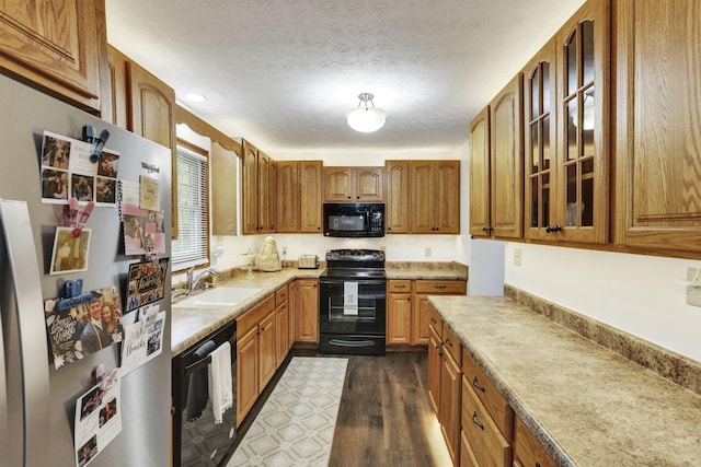 kitchen featuring brown cabinets, a sink, light countertops, black appliances, and glass insert cabinets