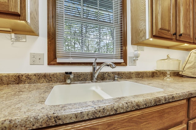 room details featuring a sink, brown cabinetry, and light stone countertops