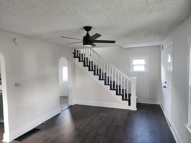 entrance foyer featuring ceiling fan, visible vents, arched walkways, stairway, and dark wood-style floors