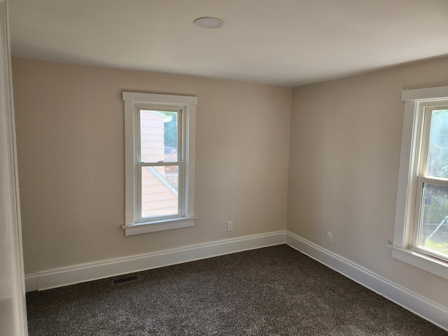 unfurnished room featuring baseboards, dark colored carpet, and visible vents