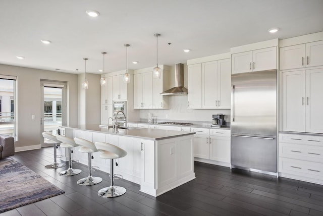 kitchen with appliances with stainless steel finishes, wall chimney range hood, wood tiled floors, a sink, and recessed lighting
