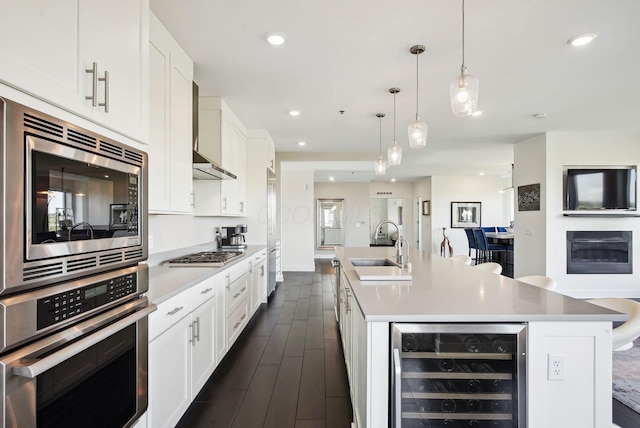 kitchen featuring wine cooler, appliances with stainless steel finishes, a sink, a center island with sink, and white cabinetry