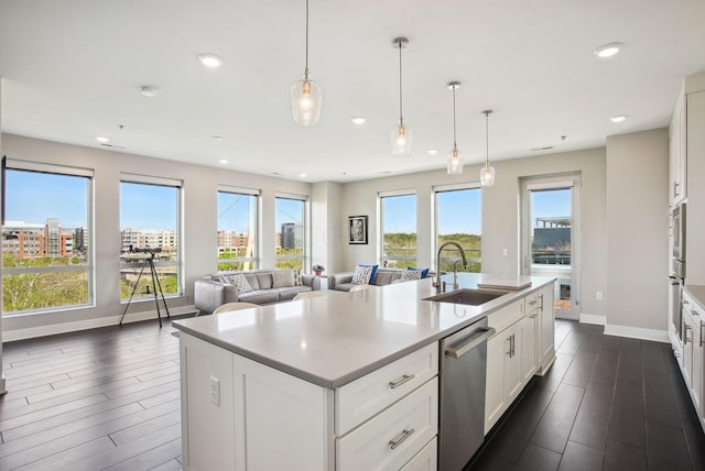 kitchen with stainless steel appliances, a sink, baseboards, white cabinets, and open floor plan