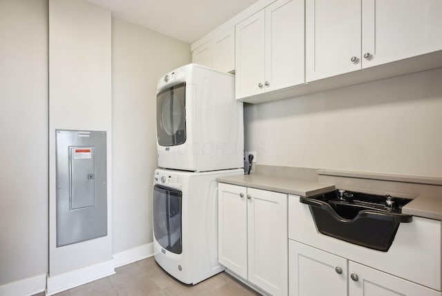 laundry area with stacked washer and clothes dryer, cabinet space, baseboards, light tile patterned floors, and electric panel