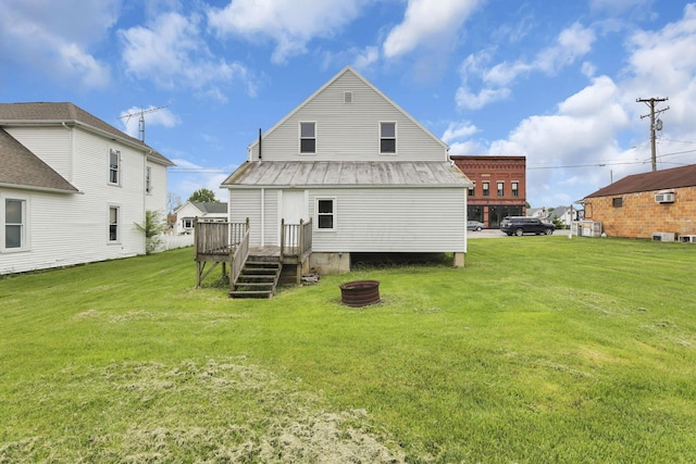 rear view of property with metal roof, a wooden deck, a lawn, and a fire pit