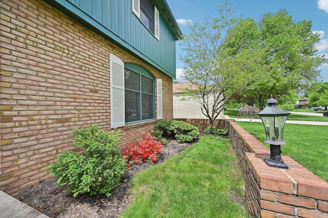 view of property exterior featuring brick siding, a lawn, and board and batten siding